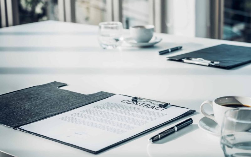 Close up business contract paper on meeting room table with pen and coffee cup in sun light shadow with green plant at office,business agreement concept
